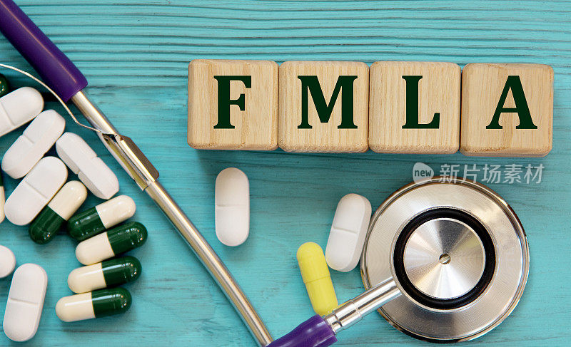 FMLA -首字母缩略词，在蓝色背景的木块上，用听诊器和药片
